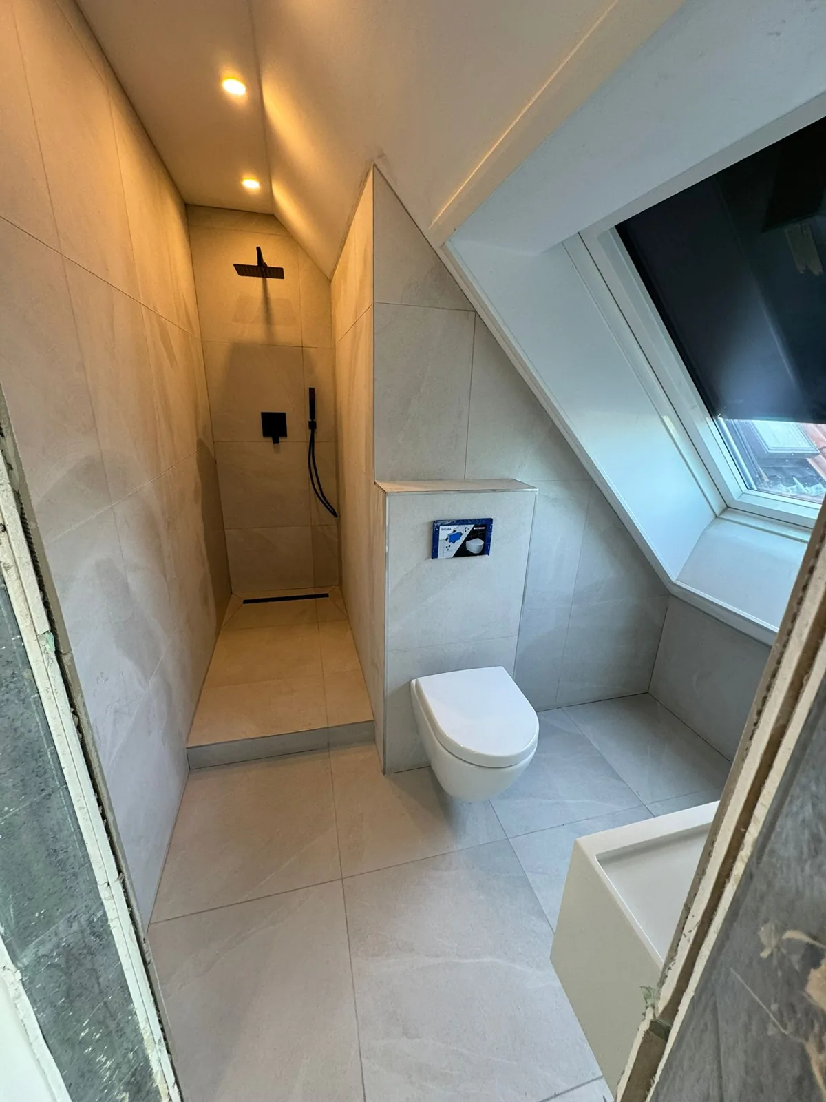 Attic ensuite with large-format grey tiles and black rainfall shower
