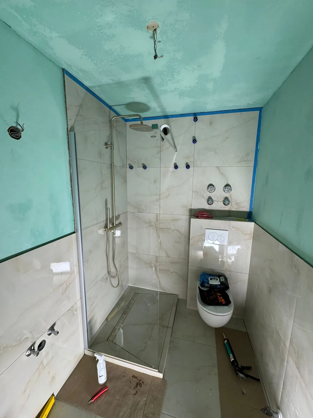 Marble-look walk-in shower with brass rainfall column and glass screen