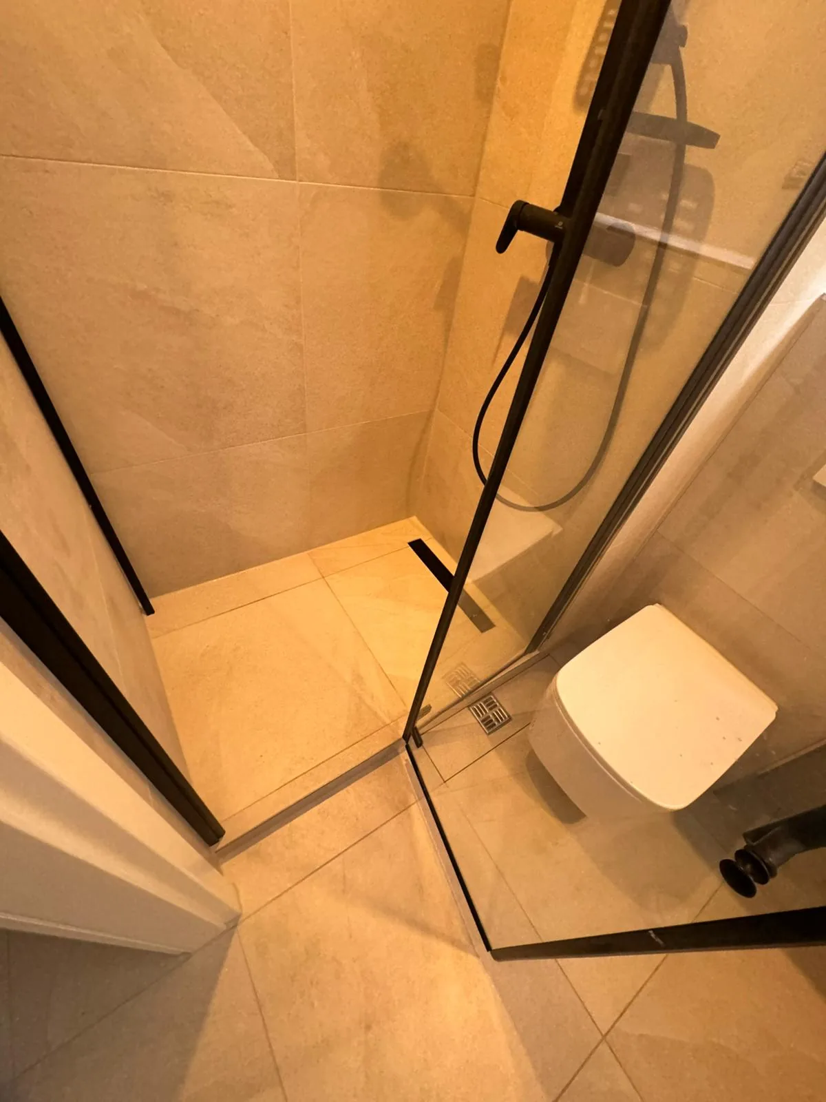Beige tiled walk-in shower with matte-black fixtures and wall-hung WC