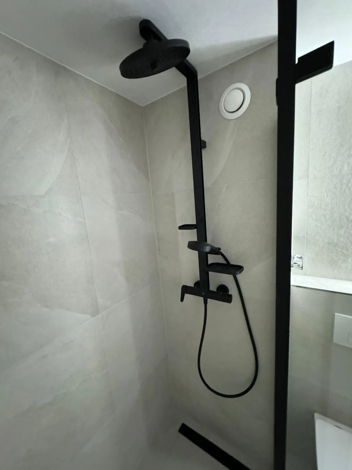 Black shower column on grey marbled tile with glass screen